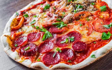 Mozzarella peynirli, jambonlu, domates soslu, salamlı, pastırmalı, mantarlı, biberli, baharatlı ve taze fesleğenli pizza. İtalyan pizzası ahşap masa arkasında