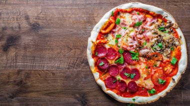 Mozzarella peynirli, jambonlu, domates soslu, salamlı, pastırmalı, mantarlı, biberli, baharatlı ve taze fesleğenli pizza. İtalyan pizzası ahşap masa arkasında