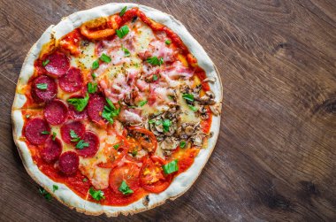 Mozzarella peynirli, jambonlu, domates soslu, salamlı, pastırmalı, mantarlı, biberli, baharatlı ve taze fesleğenli pizza. İtalyan pizzası ahşap masa arkasında