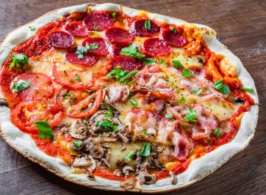 Mozzarella peynirli, jambonlu, domates soslu, salamlı, pastırmalı, mantarlı, biberli, baharatlı ve taze fesleğenli pizza. İtalyan pizzası ahşap masa arkasında