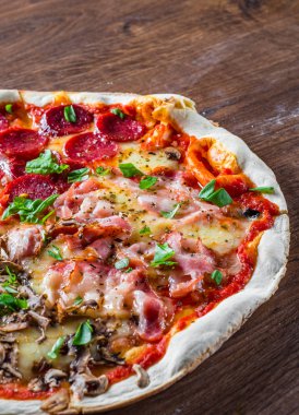 Mozzarella peynirli, jambonlu, domates soslu, salamlı, pastırmalı, mantarlı, biberli, baharatlı ve taze fesleğenli pizza. İtalyan pizzası ahşap masa arkasında