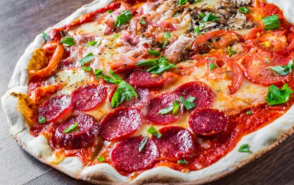 Mozzarella peynirli, jambonlu, domates soslu, salamlı, pastırmalı, mantarlı, biberli, baharatlı ve taze fesleğenli pizza. İtalyan pizzası ahşap masa arkasında