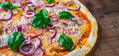Pizza Mozzarella peynir, jambon, domates sosu, soğan, biber, Baharat ve Taze fesleğen ile. Ahşap masa arka planda İtalyan pizza