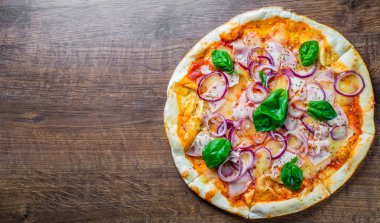 Pizza Mozzarella peynir, jambon, domates sosu, soğan, biber, Baharat ve Taze fesleğen ile. Ahşap masa arka planda İtalyan pizza