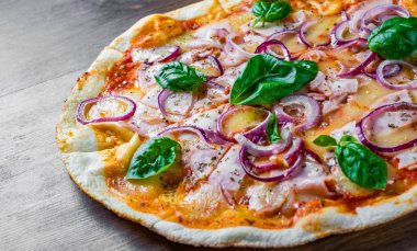 Pizza Mozzarella peynir, jambon, domates sosu, soğan, biber, Baharat ve Taze fesleğen ile. Ahşap masa arka planda İtalyan pizza