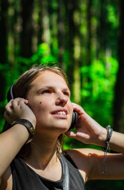 Uzun saçlı genç genç esmer kız Açık portre. Ormanda kulaklıkla müzik dinleyen mutlu genç kadın.