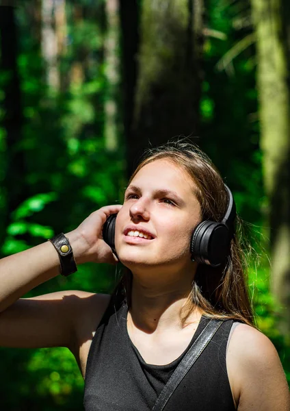 長い髪を持つ若いティーンエイジャーブルネットの女の子の屋外の肖像画 森の中でヘッドフォンで音楽を聴く幸せな若い女性 — ストック写真