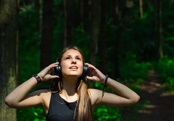 長い髪を持つ若いティーンエイジャーブルネットの女の子の屋外の肖像画 森の中でヘッドフォンで音楽を聴く幸せな若い女性 — ストック写真