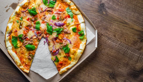 Pizza with Mozzarella cheese, onion, tuna fish, tomato sauce, pepper, basil. Italian pizza in the delivery cardboard box on wooden table background