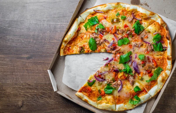 Pizza with Mozzarella cheese, onion, tuna fish, tomato sauce, pepper, basil. Italian pizza in the delivery cardboard box on wooden table background