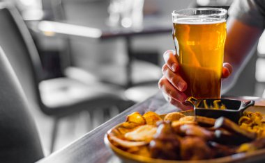 bar veya pub ahşap masa arka plan üzerinde aperatifler ile soğuk bira ve tabak cam ile adam el