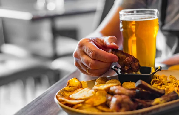 man hand with glass of cold beer and plate with snacks on wooden table background on bar or pub