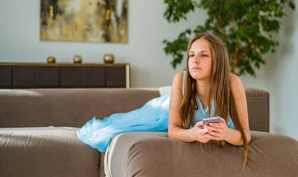 自宅のソファに横たわっている長い髪を持つ若いティーンエイジャーブルネットの女の子の肖像画は スマートフォンを使用して楽しみを持っています — ストック写真