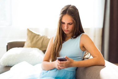 evde kanepede oturan uzun saçlı genç genç esmer kız portresi akıllı telefon kullanarak eğlenin