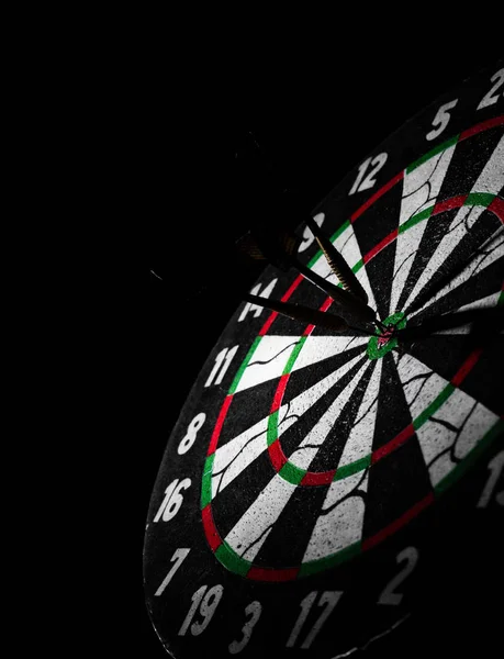 Dartboard with dart arrow hitting the center on a dark black background with copy space.