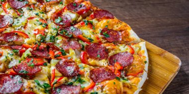 Mozzarella peynirli Pepperoni Pizza, salam, biber. Baharatlar ve taze fesleğen. Ahşap masa arka planda İtalyan pizza