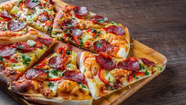 Mozzarella peynirli Pepperoni Pizza, salam, biber. Baharatlar ve taze fesleğen. Ahşap masa arka planda İtalyan pizza