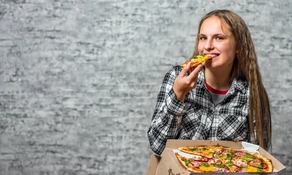 長い髪を持つ若いティーンエイジャーブルネットの女の子の肖像画は 灰色の壁の背景にピザのスライスを食べる — ストック写真