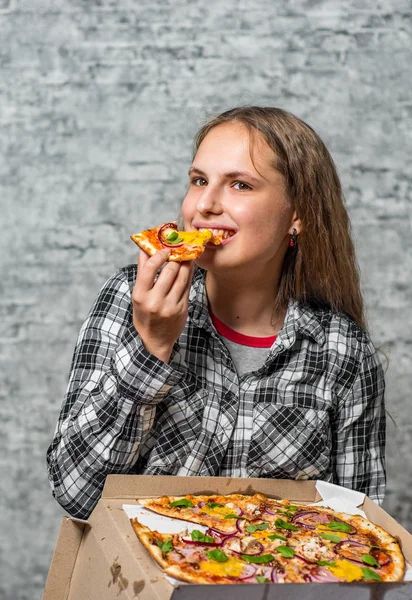 長い髪を持つ若いティーンエイジャーブルネットの女の子の肖像画は 灰色の壁の背景にピザのスライスを食べる — ストック写真