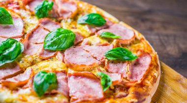 Pizza Mozzarella peynir, jambon, domates sosu, biber, Baharat ve Taze fesleğen ile. Ahşap masa arka planda İtalyan pizza