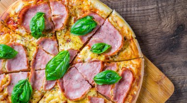 Pizza Mozzarella peynir, jambon, domates sosu, biber, Baharat ve Taze fesleğen ile. Ahşap masa arka planda İtalyan pizza
