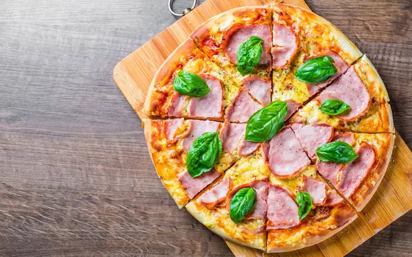 Pizza Mozzarella peynir, jambon, domates sosu, biber, Baharat ve Taze fesleğen ile. Ahşap masa arka planda İtalyan pizza