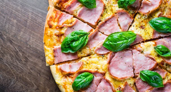 Pizza Mozzarella peynir, jambon, domates sosu, biber, Baharat ve Taze fesleğen ile. Ahşap masa arka planda İtalyan pizza