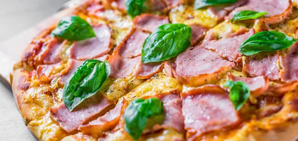 Pizza Mozzarella peynir, jambon, domates sosu, biber, Baharat ve Taze fesleğen ile. Ahşap masa arka planda İtalyan pizza