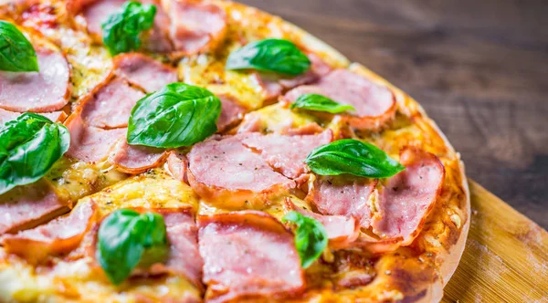 Pizza Mozzarella peynir, jambon, domates sosu, biber, Baharat ve Taze fesleğen ile. Ahşap masa arka planda İtalyan pizza