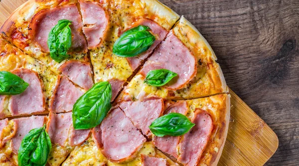 Pizza Mozzarella peynir, jambon, domates sosu, biber, Baharat ve Taze fesleğen ile. Ahşap masa arka planda İtalyan pizza