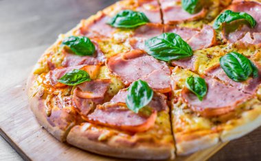 Pizza Mozzarella peynir, jambon, domates sosu, biber, Baharat ve Taze fesleğen ile. Ahşap masa arka planda İtalyan pizza