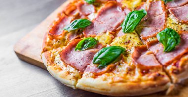 Pizza Mozzarella peynir, jambon, domates sosu, biber, Baharat ve Taze fesleğen ile. Ahşap masa arka planda İtalyan pizza