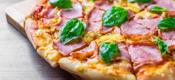 Pizza Mozzarella peynir, jambon, domates sosu, biber, Baharat ve Taze fesleğen ile. Ahşap masa arka planda İtalyan pizza