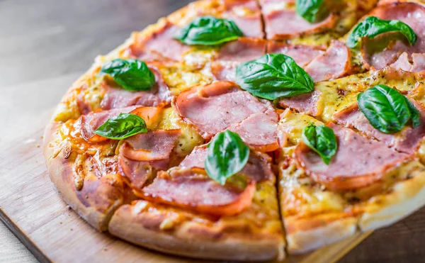Pizza Mozzarella peynir, jambon, domates sosu, biber, Baharat ve Taze fesleğen ile. Ahşap masa arka planda İtalyan pizza