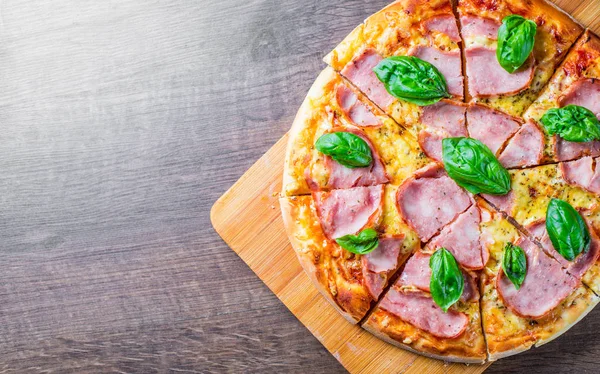 Pizza Mozzarella peynir, jambon, domates sosu, biber, Baharat ve Taze fesleğen ile. Ahşap masa arka planda İtalyan pizza