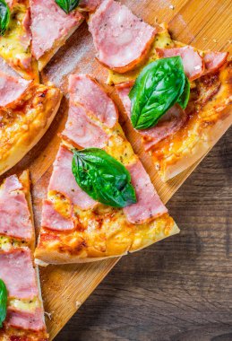 Pizza Mozzarella peynir, jambon, domates sosu, biber, Baharat ve Taze fesleğen ile. Ahşap masa arka planda İtalyan pizza