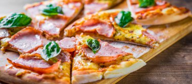 Pizza Mozzarella peynir, jambon, domates sosu, biber, Baharat ve Taze fesleğen ile. Ahşap masa arka planda İtalyan pizza