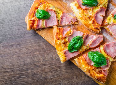 Pizza Mozzarella peynir, jambon, domates sosu, biber, Baharat ve Taze fesleğen ile. Ahşap masa arka planda İtalyan pizza