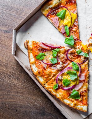 Mozzarella peynir, jambon, pastırma, Domates sosu, biber, Baharat ve soğan ile Pizza dilim. Ahşap masa arka plan üzerinde kutusunda İtalyan pizza