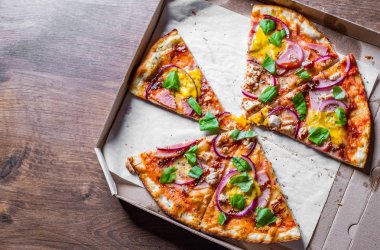 Mozzarella peynir, jambon, pastırma, Domates sosu, biber, Baharat ve soğan ile Pizza dilim. Ahşap masa arka plan üzerinde kutusunda İtalyan pizza