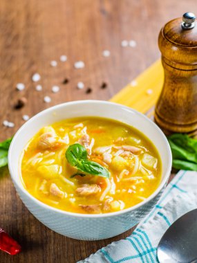 Erişteli tavuk çorbası ve ahşap masa arkasındaki beyaz kasede sebze.