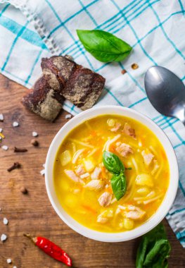 Erişteli tavuk çorbası ve ahşap masa arkasındaki beyaz kasede sebze.