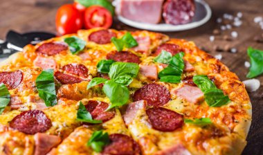 Mozzarella peyniri, salam, jambon, Baharatlar ve Taze fesleğenli Pepperoni Pizza. Ahşap masa arka planda İtalyan pizza