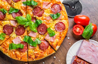 Mozzarella peyniri, salam, jambon, Baharatlar ve Taze fesleğenli Pepperoni Pizza. Ahşap masa arka planda İtalyan pizza