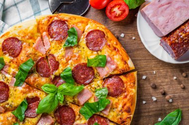 Mozzarella peyniri, salam, jambon, Baharatlar ve Taze fesleğenli Pepperoni Pizza. Ahşap masa arka planda İtalyan pizza