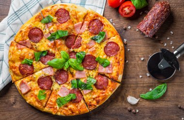 Mozzarella peyniri, salam, jambon, Baharatlar ve Taze fesleğenli Pepperoni Pizza. Ahşap masa arka planda İtalyan pizza