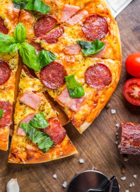 Mozzarella peyniri, salam, jambon, Baharatlar ve Taze fesleğenli Pepperoni Pizza. Ahşap masa arka planda İtalyan pizza