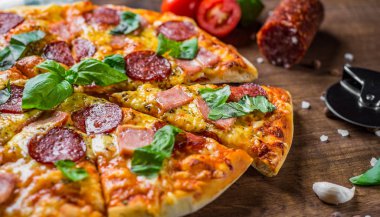 Mozzarella peyniri, salam, jambon, Baharatlar ve Taze fesleğenli Pepperoni Pizza. Ahşap masa arka planda İtalyan pizza
