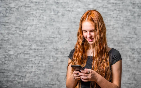 Kızıl Saçlı Uzun Saçlı Gri Duvarda Akıllı Telefonu Olan Genç — Stok fotoğraf