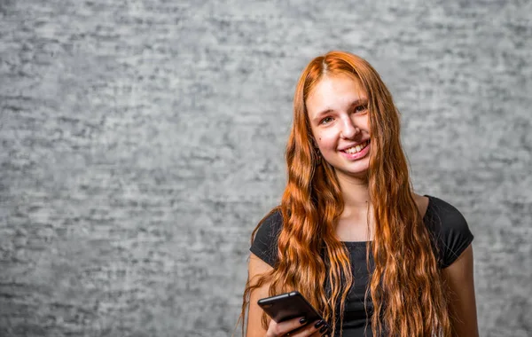 若いですティーンRedhead女の子とともに長い髪とスマートフォン上の灰色の壁の背景 — ストック写真